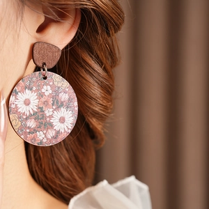 Close-up of vintage wooden round earrings with floral patterns worn by a model