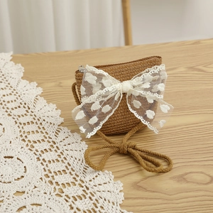 Détail d'un sac bandoulière en paille avec nœud en dentelle blanche sur bois rustique