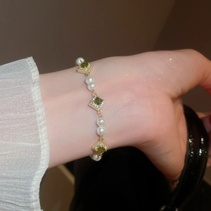 Close-up of gold chain bracelet with green zircon square stones and white pearls