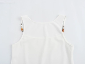 Close-up of a white camisole top featuring decorative metal and brown beaded shoulder straps
