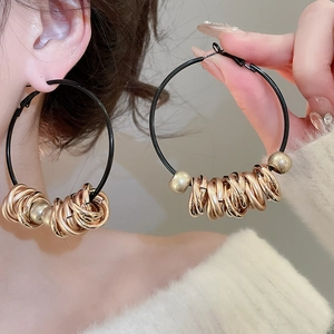 Close-up of model wearing exaggerated black round hoop earrings with golden bead details