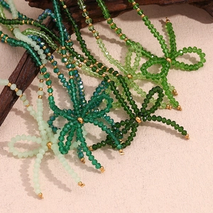 Green crystal bead necklace with butterfly bow pendant and gold accents on a textured surface