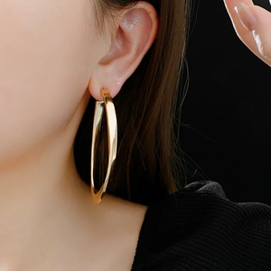 Close-up of a model wearing large golden twisted oval hoop earrings against a black background