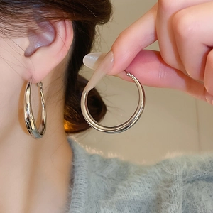 Macro detail of high-polish silver C-shaped hoop earrings on model showing mirror finish