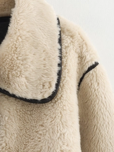 Dettaglio cappotto in ecopelliccia beige con profili neri a contrasto su bavero e spalla