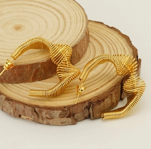 Macro shot of gold spiral wire earrings on wooden stands with artistic C-shaped design