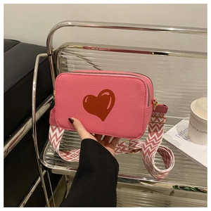Close-up of pink heart crossbody bag with chevron pattern wide woven shoulder strap