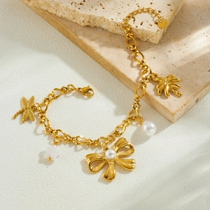 Gold stainless steel bracelet with pearl bow, dragonfly, and palm tree charms on stone