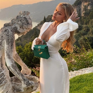 Elegant emerald green leather handbag paired with a slim-fit white knit dress at sunset
