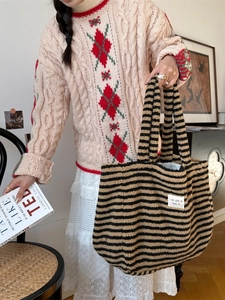Brown and black striped plush tote bag with fabric label shown in a lifestyle setting