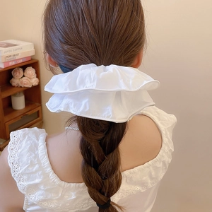 Détail d'un chouchou en tissu froissé blanc porté sur une queue de cheval tressée brune