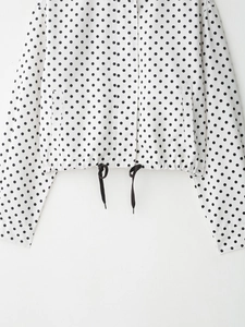 Détail d'une veste à pois montrant l'ourlet à cordon et les poches latérales sur blanc