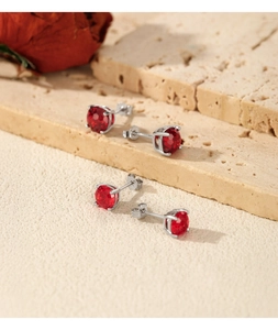 Macro detail of four-prong red gemstone stud earrings on a textured stone surface