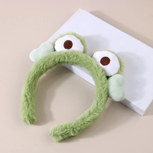Close-up of soft green plush headband with cute frog eyes on white display stand