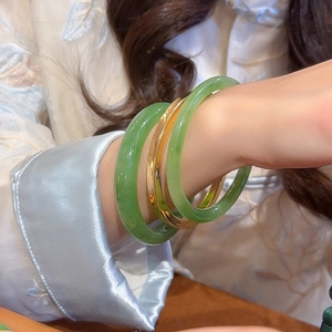 Close-up of stacked jade-like green resin bangles and a polished gold metal bracelet