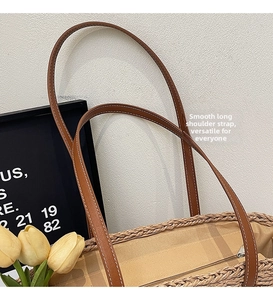 Detail of hand-woven straw tote bag featuring leather shoulder straps and zipper closure