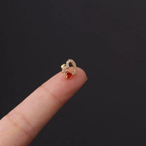 Macro shot of gold-plated heart cartilage stud earring with cubic zirconia and red enamel