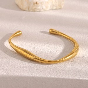 Detail of minimalist 18K gold plated stainless steel bangle with fluid irregular design