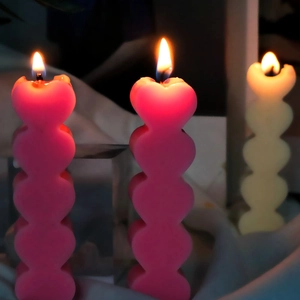 Candele profumate a forma di cuore impilate in rosa e beige su sfondo di tessuto scuro