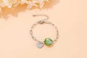 Detail of silver paperclip bracelet featuring a green geometric bead and heart charm