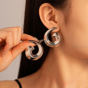 Model wearing silver chunky spiral hoop earrings with glossy geometric metallic finish