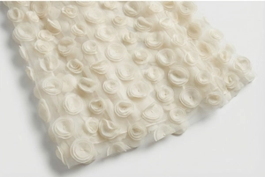 Close-up of elegant 3D rose petal embroidery on ivory mesh fabric of the evening gown