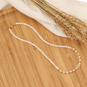 Detail of beaded necklace with white pearls and pink flower pendant on wooden tray