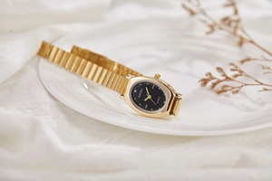 Close-up of elegant gold oval watch with black dial on a white porcelain plate