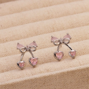 Dettaglio di orecchini a fiocco argentati con cristalli a cuore rosa su tessuto beige