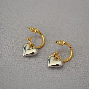 Close-up of gold ear hooks with 3D silver heart pendants on a textured grey surface