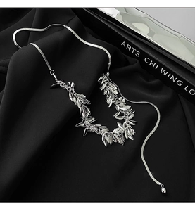 Silver wheat ear sequin necklace displayed on elegant black pleated satin fabric background