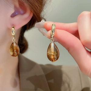 Detail of amber resin teardrop earrings with golden metal loops on elegant model