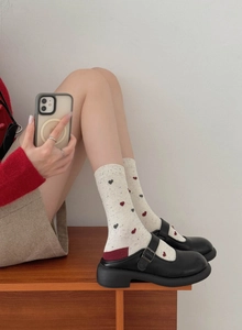 Close-up of cream knit socks with red hearts paired with black Mary Jane shoes