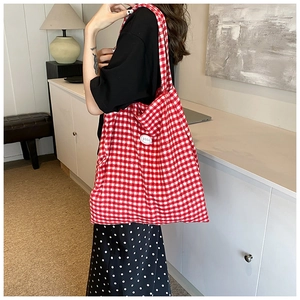 Detail of red and white checkered canvas tote bag worn by model in bright interior setting