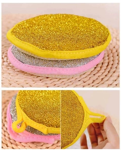 Close-up of circular gold and silver scrubbing sponges with hanging loops and pink fabric edges