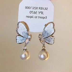 Detail of silver butterfly earrings with sparkling crystals and hanging round white pearls
