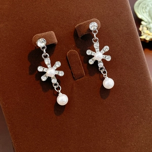 Detailed close-up of crystal flower earrings with teardrop pearls on a brown velvet stand