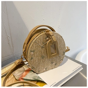Detail view of woven straw bag with floral embroidery and PU leather handle on a table
