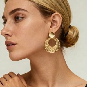 Detail of gold circular woven texture earrings worn by a model in a close-up shot