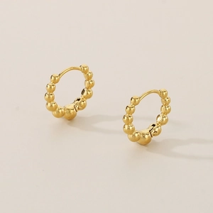 Close-up detail of golden titanium steel bead hoop earrings on a warm beige background