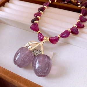 Detailed close-up of a purple heart-beaded necklace with a glittery cherry pendant