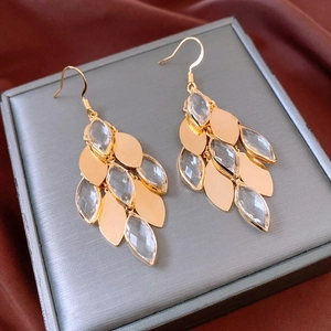 Detailed macro view of gold-plated leaf drop earrings with crystal accents on silk