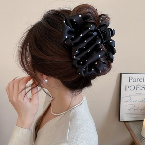 Close-up of a black and white polka dot satin hair claw clip worn in a low bun hairstyle