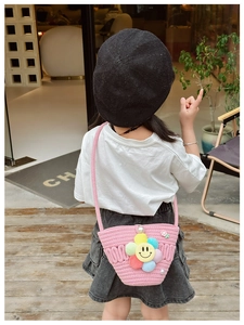 Pink woven crossbody bag for kids featuring floral smiley decor worn by a girl in a cafe