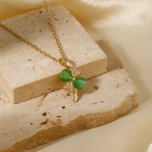 Golden clover pendant necklace with green stones and white zircons on silk background