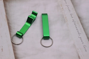 Macro detail of two green metal bottle openers with silver keyrings on a white surface