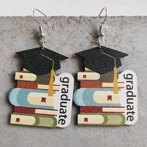 Detail of wooden graduation earrings featuring a black cap on books with graduate text