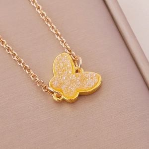Golden chain necklace with a yellow acrylic butterfly pendant on beige textured cloth