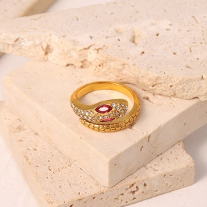 Detailed view of 18K gold snake ring with red stones and zircon on travertine stones