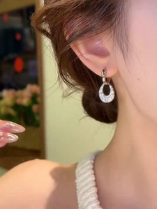 Detail of sparkling zircon teardrop earrings worn on ear with polished silver finish